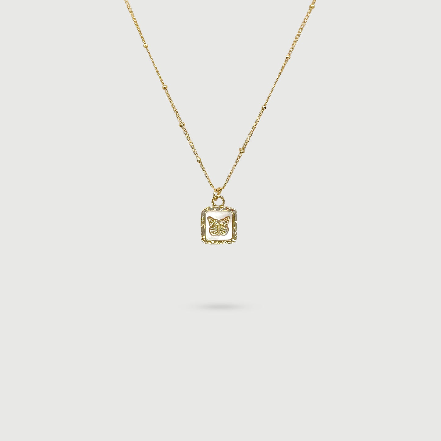 Small golden butterfly necklace on mother-of-pearl plate